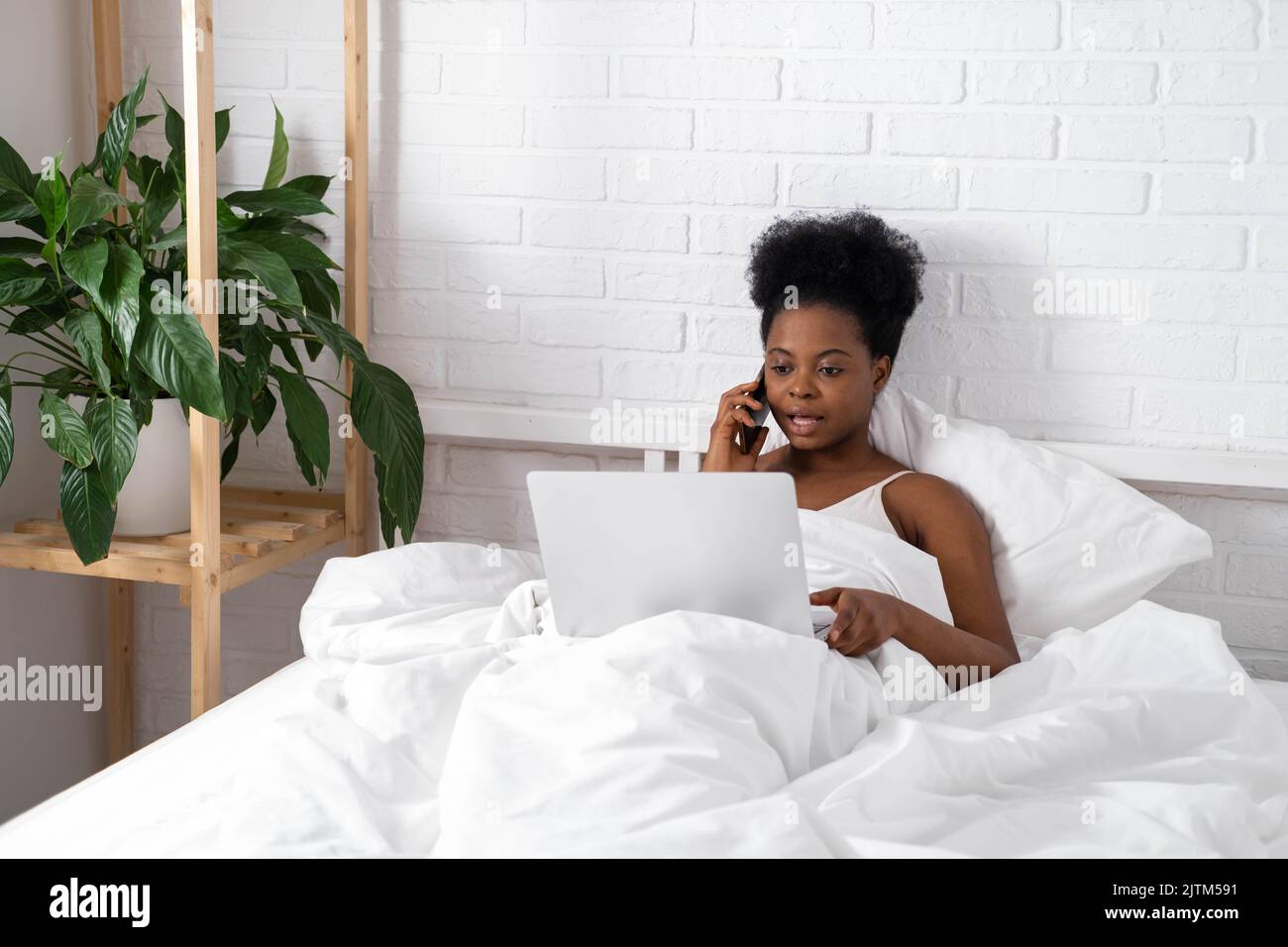 Glücklich attraktive afroamerikanische Mädchen arbeiten Büro aus der Ferne, Schwarze Frau mit Laptop-Computer und Telefon sitzen im Bett zu Hause, Distanz Stockfoto