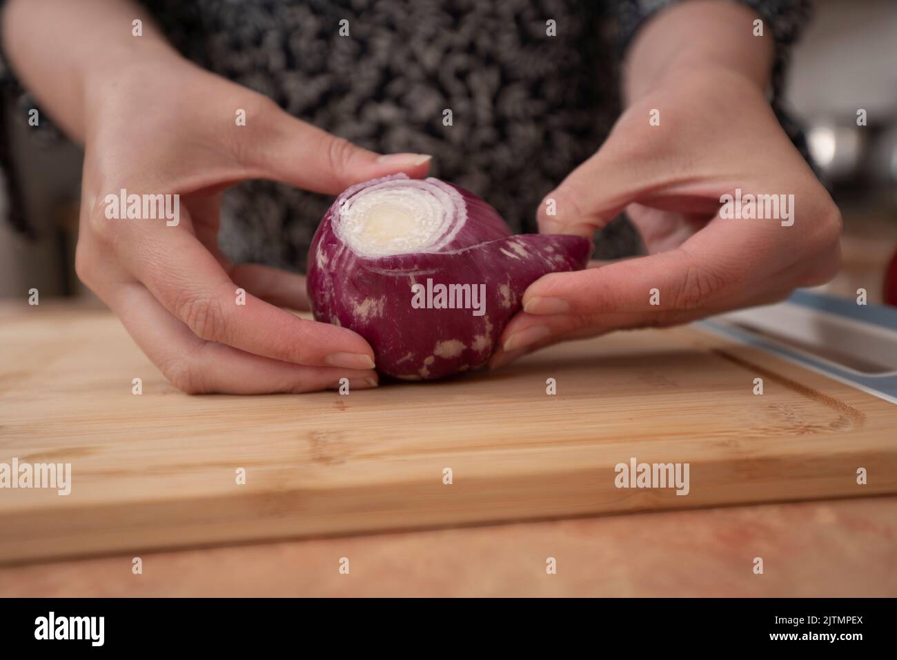 Die Hände der Frau beginnen, eine Zwiebel auf einem Holzbrett in der Küche zu schälen Stockfoto