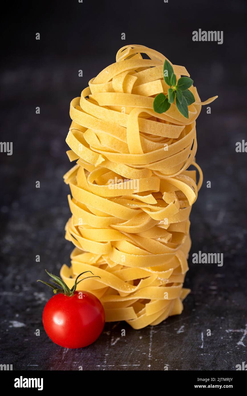 Fotos von rohen Nudeln, Tagliatelle, Fettuccine, Makro, Tomate, Oregano Stockfoto