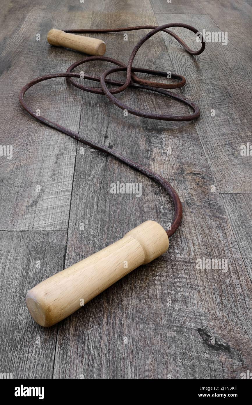 Altes Leder-Springseil mit Holzgriffen, auf einem Holzboden gewickelt Stockfoto