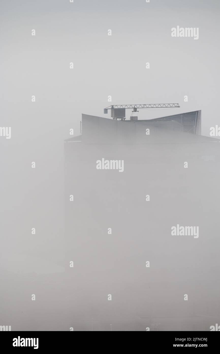 Der Gipfel des Wolkenkratzers mit Kran erscheint durch Nebel Stockfoto