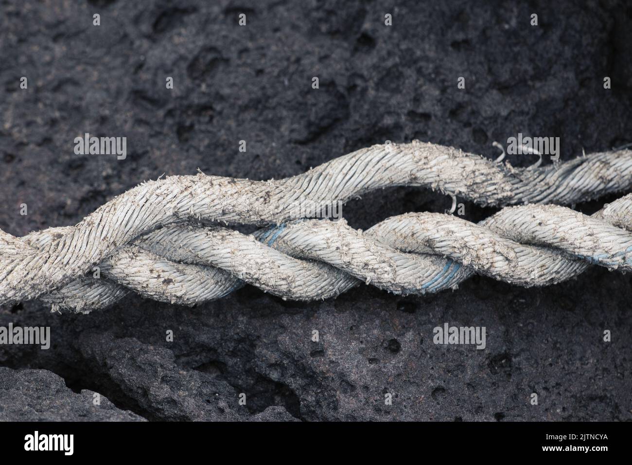 Altes weißes Seil auf schwarzem Felsen löst sich auf Stockfoto