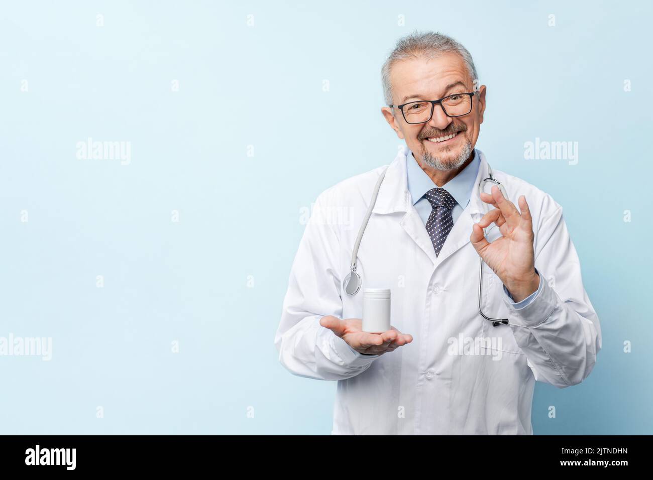Medizin, Gesundheitswesen und Berufskonzept - lächelnder, gealterter Arzt mit Stethoskop hält das Medikament, das den Daumen im Krankenhaus zeigt. Stockfoto