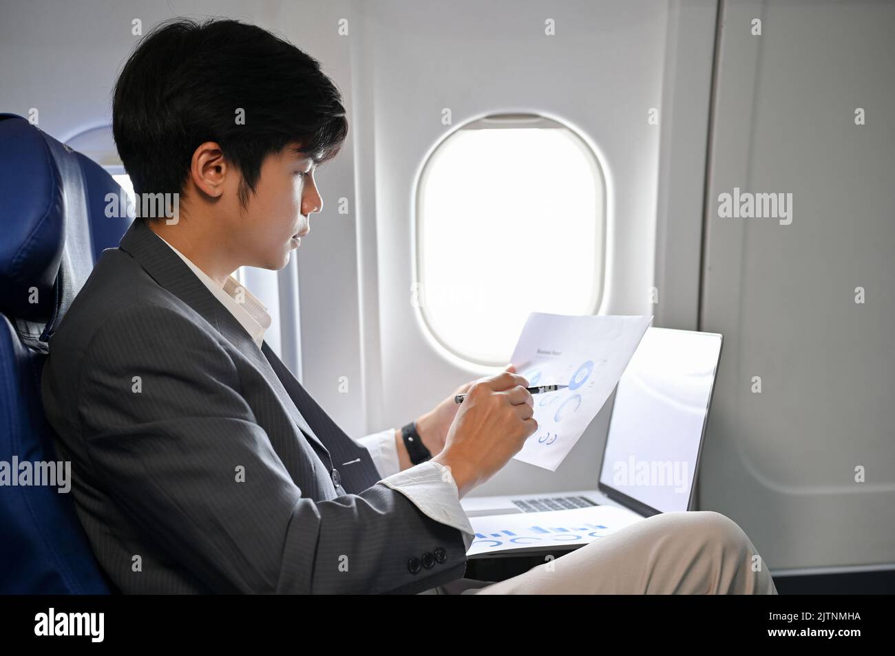 Professioneller asiatischer Geschäftsmann, der sich auf dem Flug zu seiner Geschäftsreise auf das Lesen und Analysieren eines Finanzdatenberichts konzentriert. Stockfoto