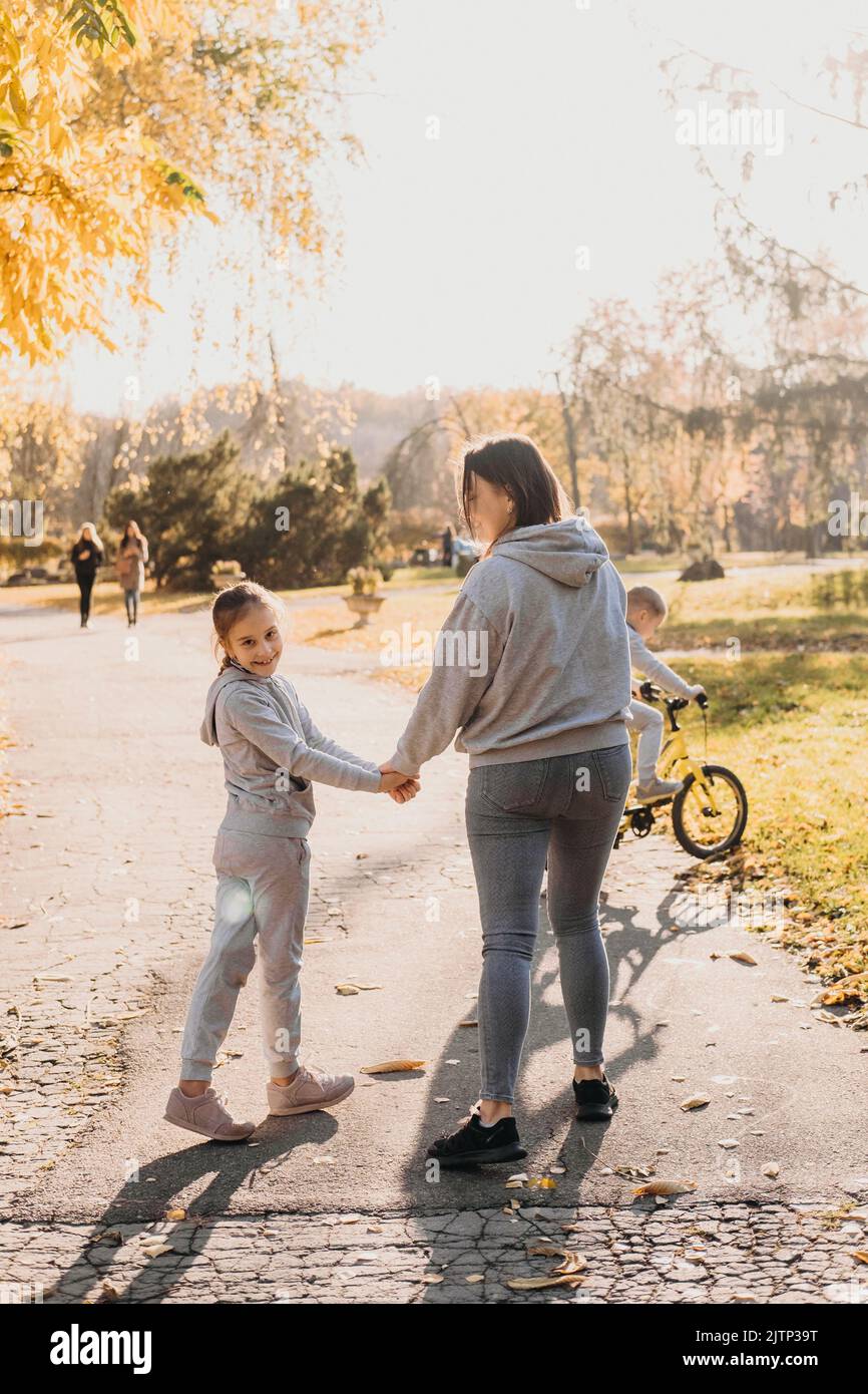 Rückansicht einer Mutter, die morgens mit ihrer Tochter im Park unterwegs war, das Mädchen drehte ihren Kopf und lächelte die Kamera an. Sommer Stockfoto