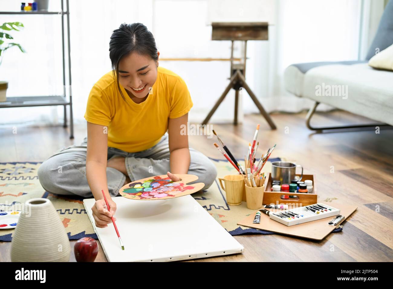 Attraktive junge asiatische Studentin konzentriert üben Zeichnen und Malen auf Leinwand zu Hause. Kreativität Hobby Konzept Stockfoto