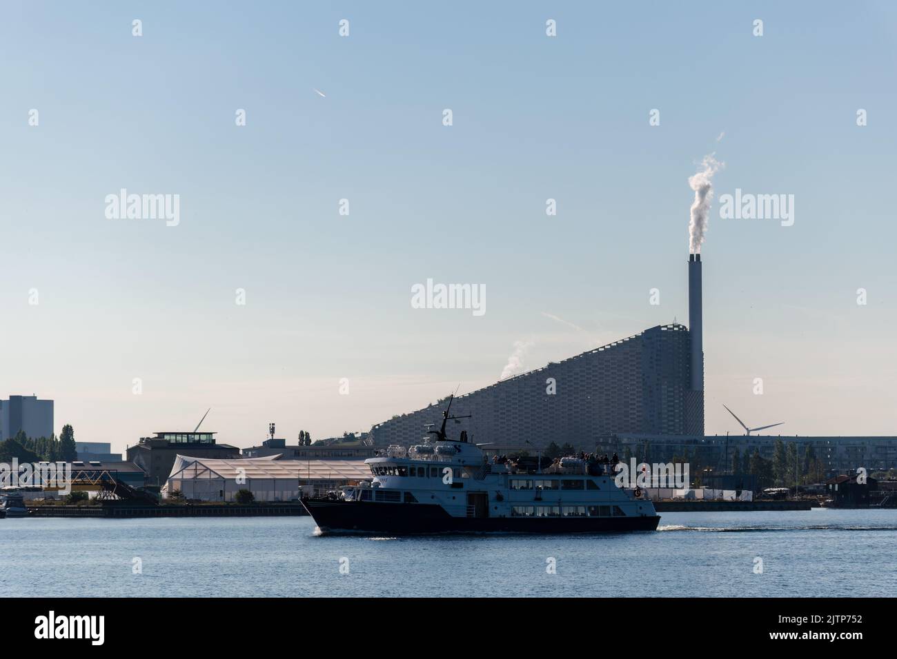 Kopenhagen, Dänemark. 13. August 2022. Eine Passagierfähre auf dem Fluss mit Amager Bakke, einem kombinierten Kraftwerk und einer Skipiste im Hintergrund Stockfoto