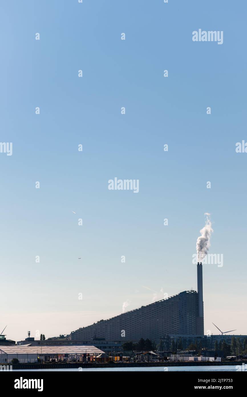 Kopenhagen, Dänemark. 13. August 2022. Amager Bakke, ein kombiniertes Kraftwerk und eine Skipiste von der anderen Seite des Flusses aus gesehen, gegen einen blauen Himmel. Stockfoto
