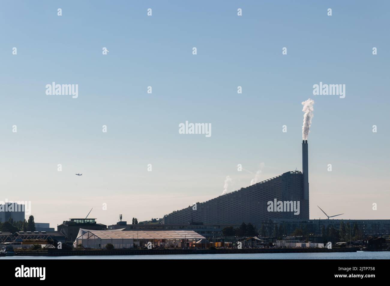 Kopenhagen, Dänemark. 13. August 2022. Amager Bakke, ein kombiniertes Kraftwerk und eine Skipiste von der anderen Seite des Flusses aus gesehen, gegen einen blauen Himmel. Stockfoto