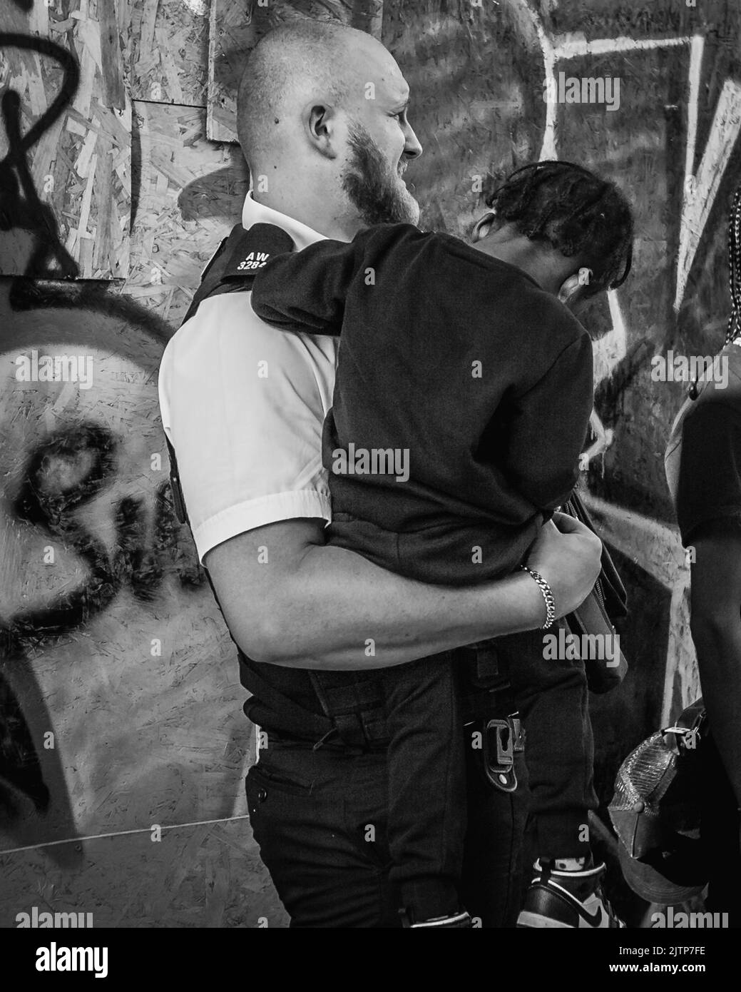 Ein schwarz-weißes Bild des Polizisten, der ein kleines Kind tröstet, das seine Eltern beim Notting Hill Carnival verloren hat. Stockfoto