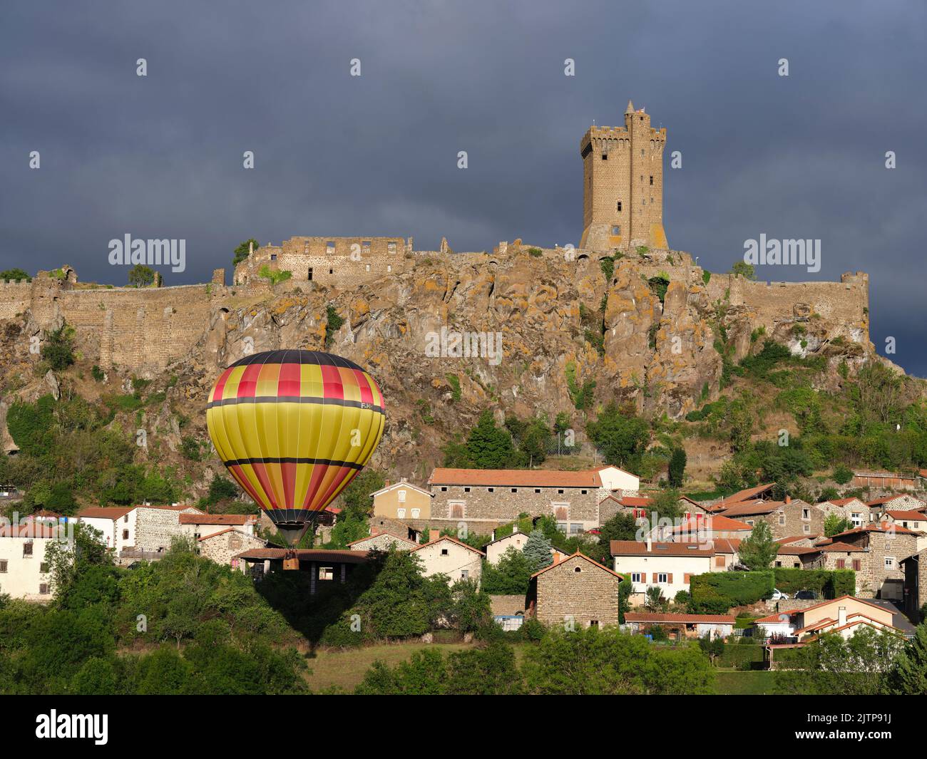 Heißluftballon, der in der Nähe einer mittelalterlichen Festung auf einer vulkanischen mesa schwebt. Polignac, Haute-Loire, Auvergne-Rhône-Alpes, Frankreich. Stockfoto