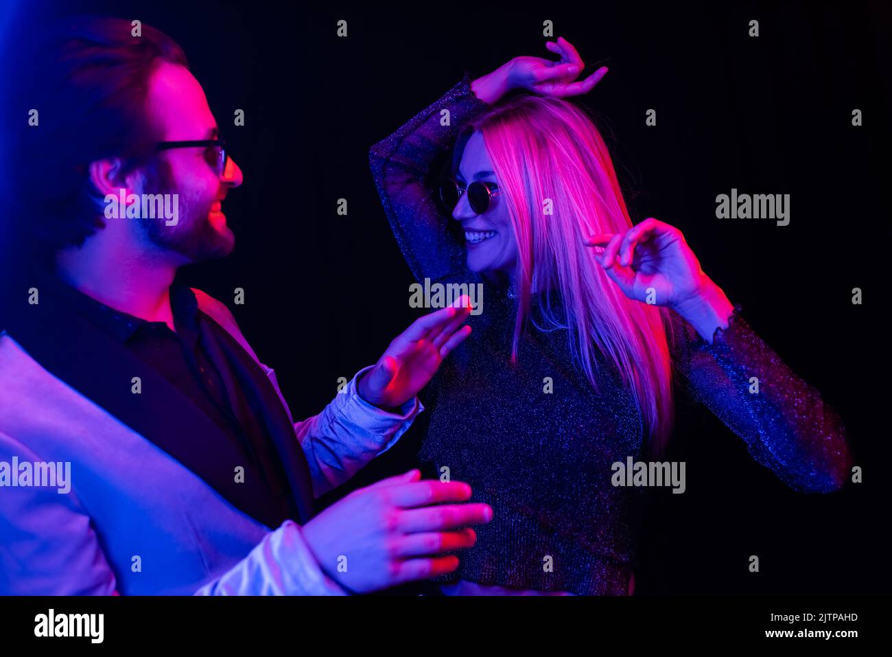 Stilvolles Coupé in Sonnenbrillen, isoliert auf Schwarz tanzend, mit farbenfroher Beleuchtung Stockfoto