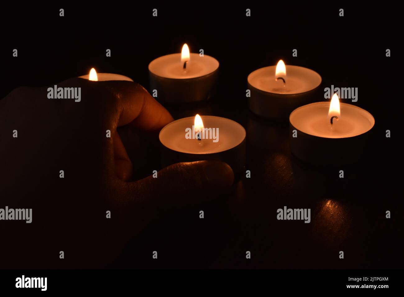 Teelicht Kerzen im dunklen Hintergrund. Hand, die eine Kerze auf den Tisch legt. Stockfoto