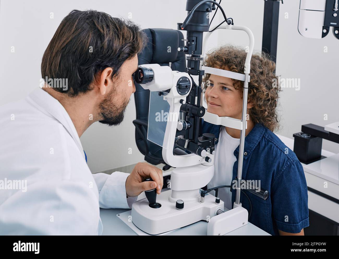 Netter Junge während der Augenuntersuchung mit binokularer Spaltlampe in der Augenklinik mit erfahrenem Optiker. Sehkorrektur bei Kindern Stockfoto