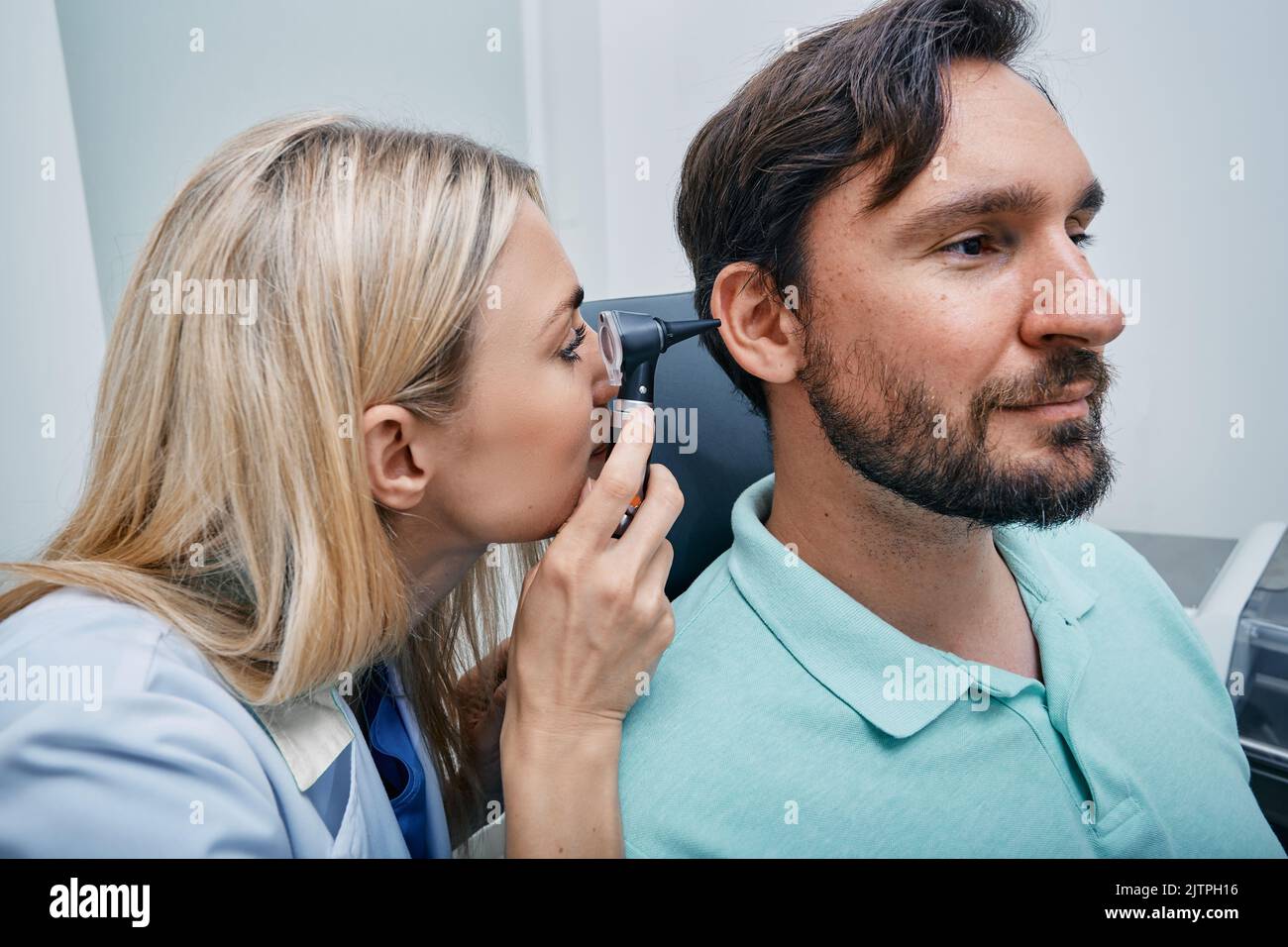 HNO-Arzt untersucht das Ohr eines erwachsenen Mannes mit Hilfe eines Otoskopes oder eines Ohrhörers in der medizinischen Einrichtung Stockfoto