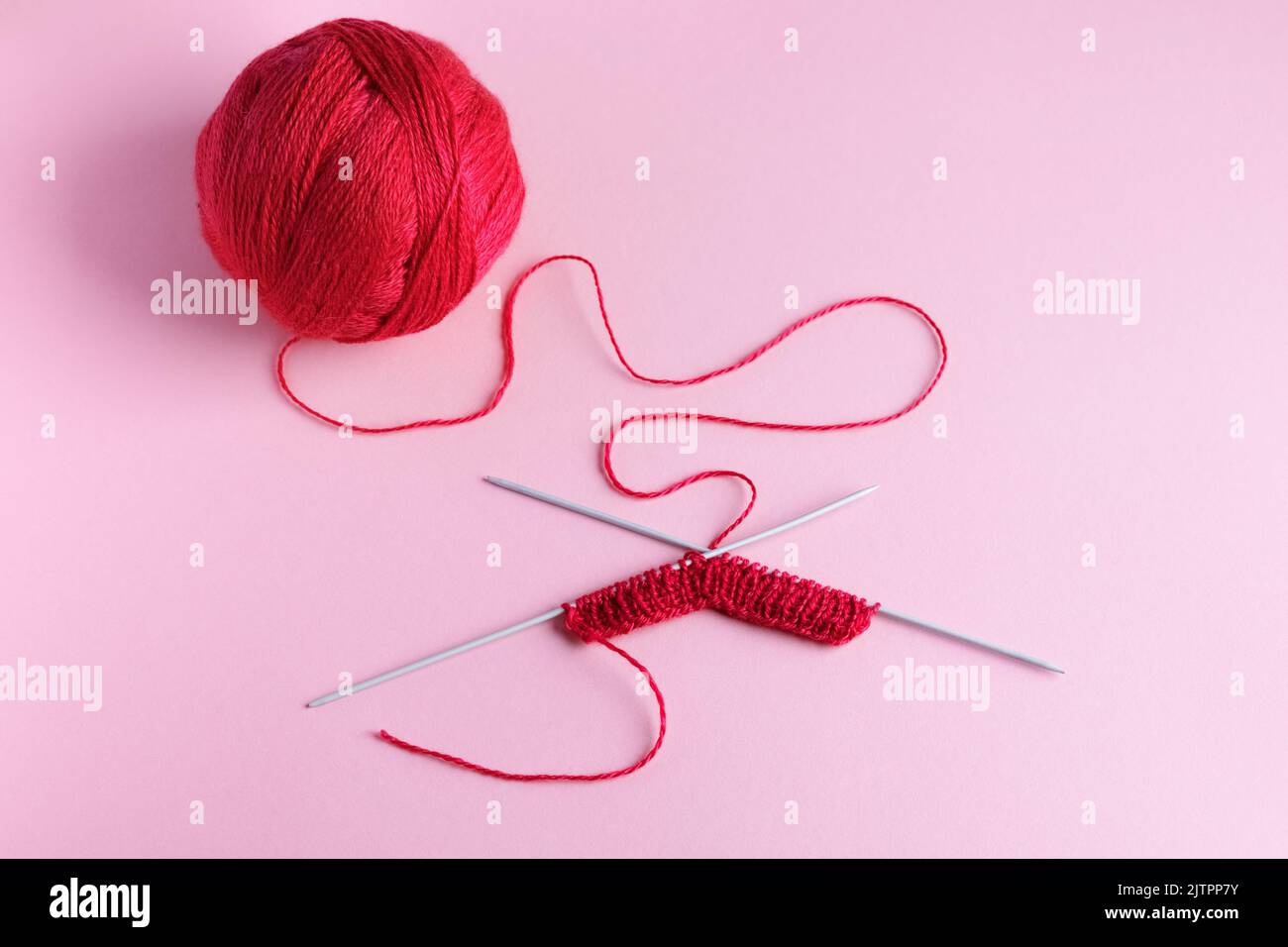 Rote Strickwolle auf rosa Hintergrund mit Stricknadeln, Hobby Stockfoto