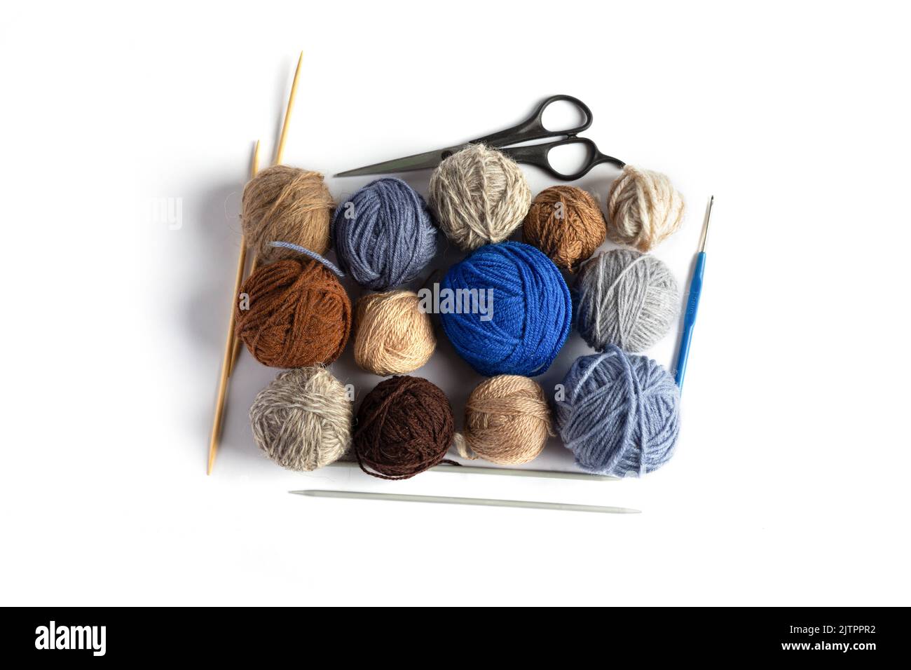 Blaue, graue und braune Strickgarnkugeln mit Schere, Häkel- und Stricknadeln auf blauem Hintergrund für Hobbys. Flach liegend Stockfoto