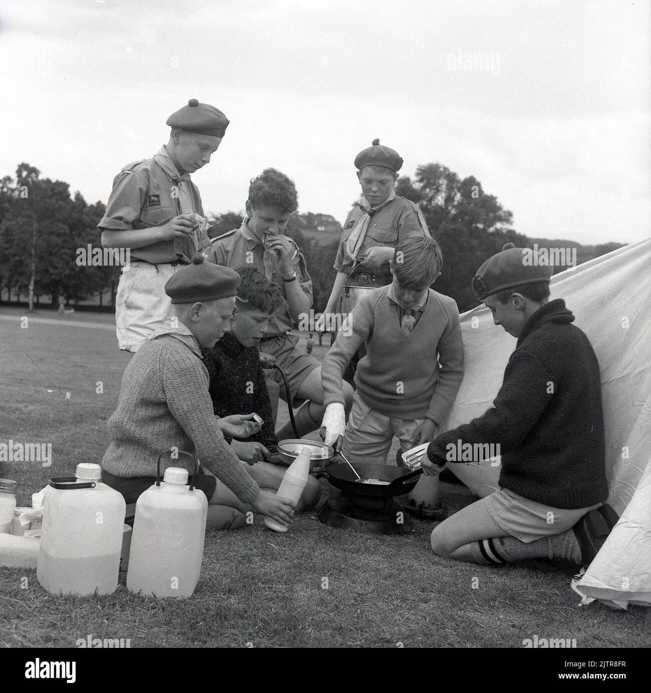 1965, historisch, Scouting in the Glen, Junge Scouts in Uniform und Barets, Kochen von Essen im Freien auf dem Gras vor einem Zelt, Schottland, Großbritannien, sieht aus wie Omelettes...... Stockfoto