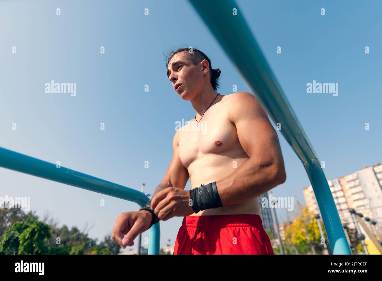 Schöner junger muskulöser Mann in roten Shorts auf dem Sportplatz im öffentlichen Park am Sommermorgen. Sport, Fitness, gesundes Lifestyle-Konzept Stockfoto