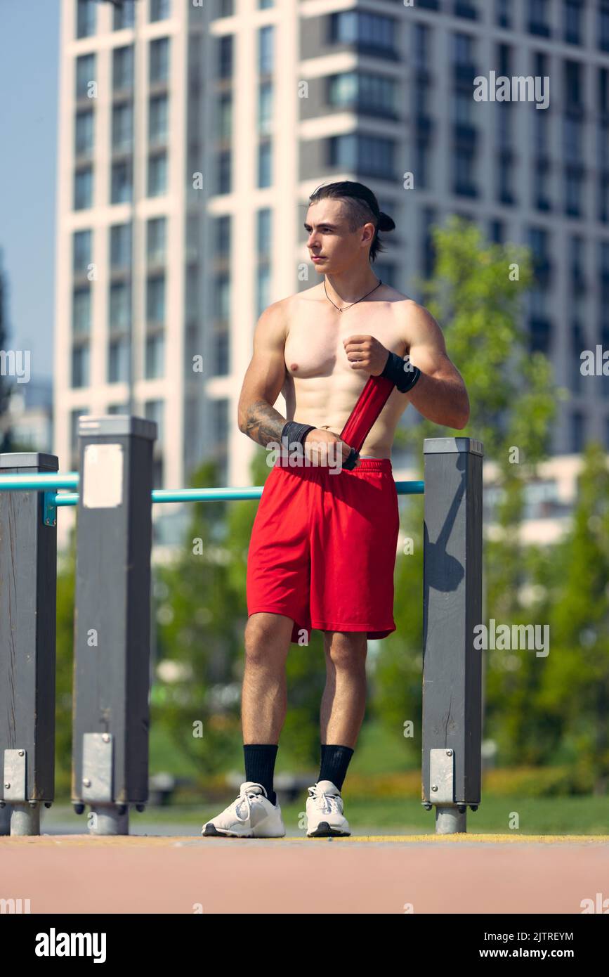 Schöner junger muskulöser Mann in roten Shorts auf dem Sportplatz im öffentlichen Park am Sommermorgen. Sport, Fitness, gesundes Lifestyle-Konzept Stockfoto