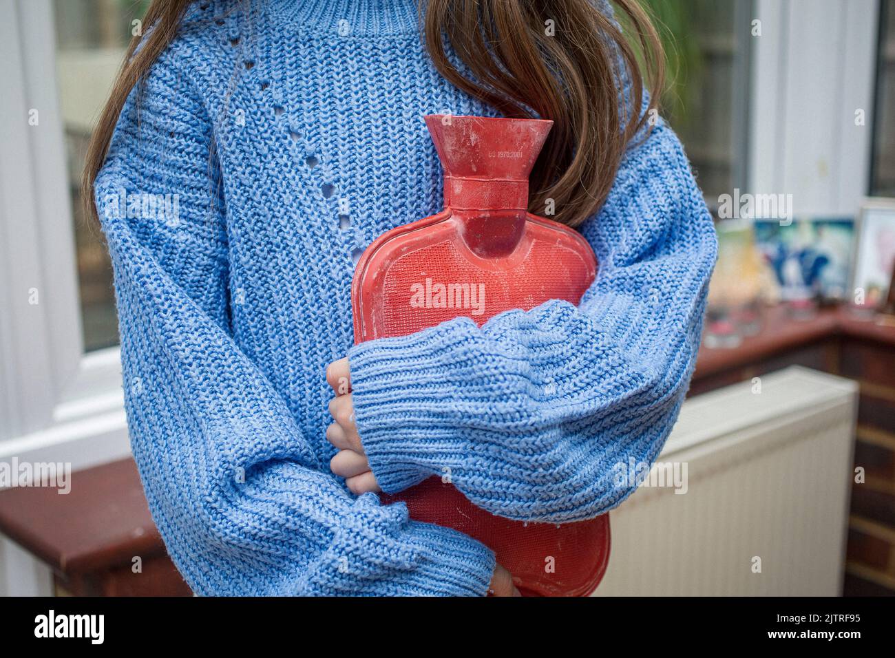 Kind hält eine Wärmflasche und versucht, sich warm zu halten, während der Kraftstoff in die Höhe schnellen wird Stockfoto