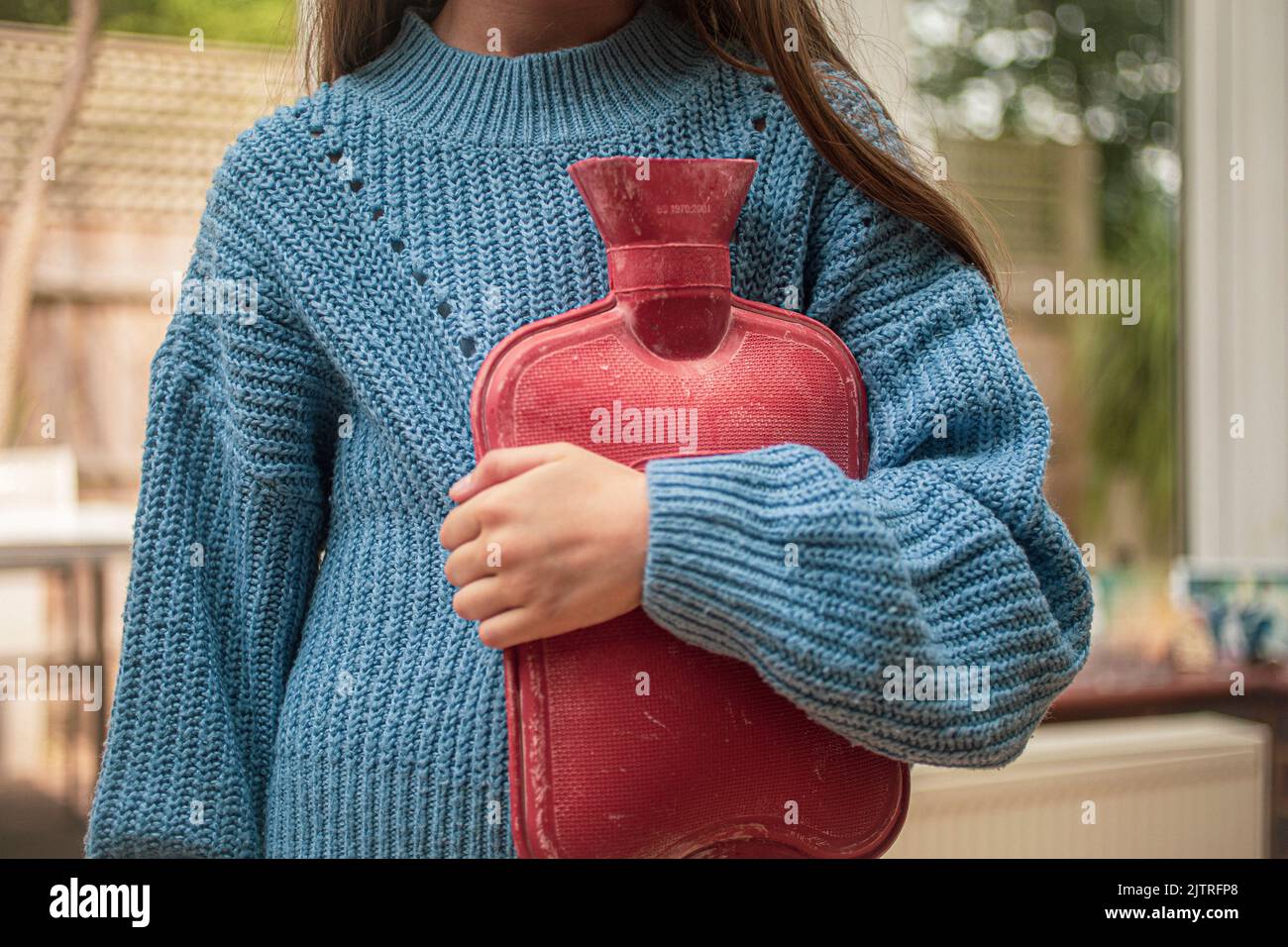 Kind hält eine Wärmflasche und versucht, sich warm zu halten, während der Kraftstoff in die Höhe schnellen wird Stockfoto