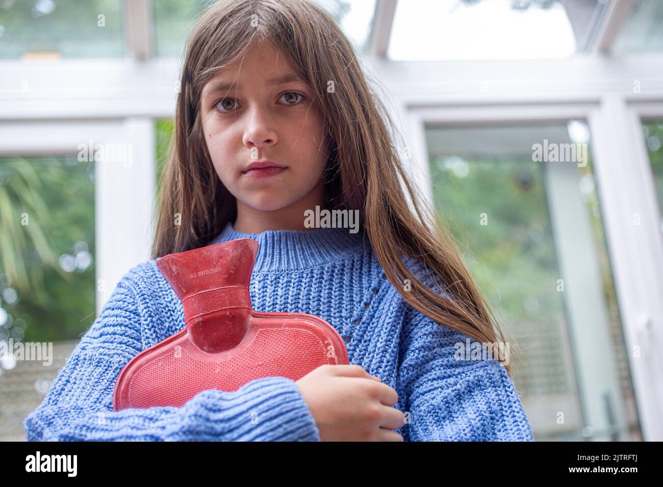 Kind hält eine Wärmflasche und versucht, sich warm zu halten, während der Kraftstoff in die Höhe schnellen wird Stockfoto