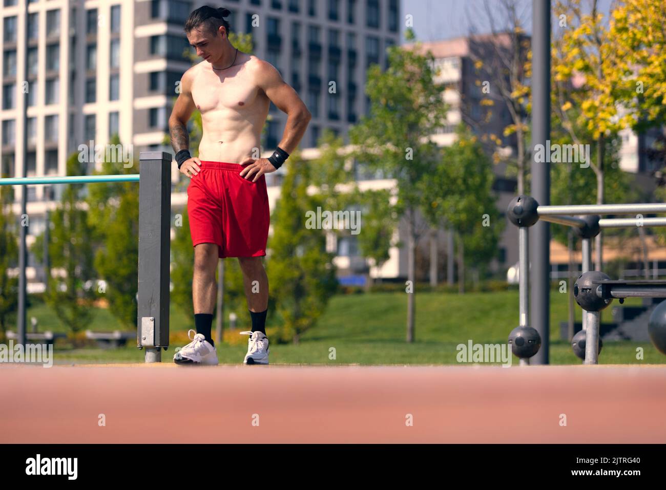 Schöner junger muskulöser Mann in roten Shorts auf dem Sportplatz im öffentlichen Park am Sommermorgen. Sport, Fitness, gesundes Lifestyle-Konzept Stockfoto