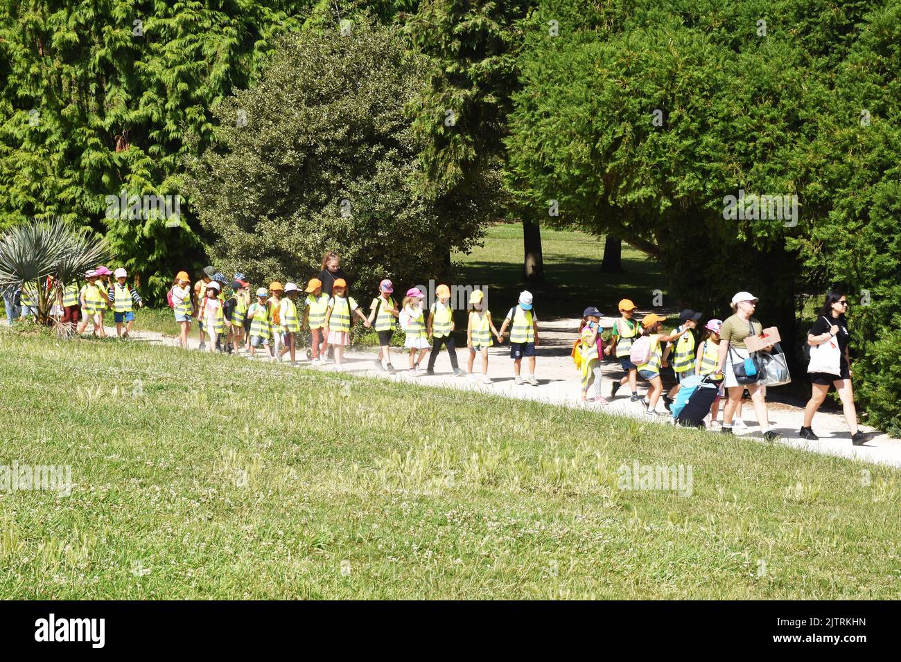 Eine Klasse von kleinen Kindern, die paarweise im Parc Montsouris, Paris, geheptet werden, alle Hände haltend und mit hoch sichtbaren Gilets und Baseballmützen getragen werden Stockfoto