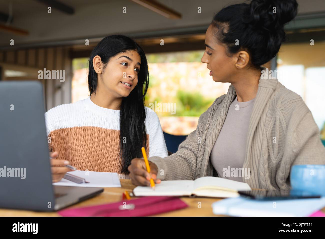 Biracial Mutter schriftlich in Buch, während Teenager Tochter auf dem Tisch zu Hause lehren Stockfoto