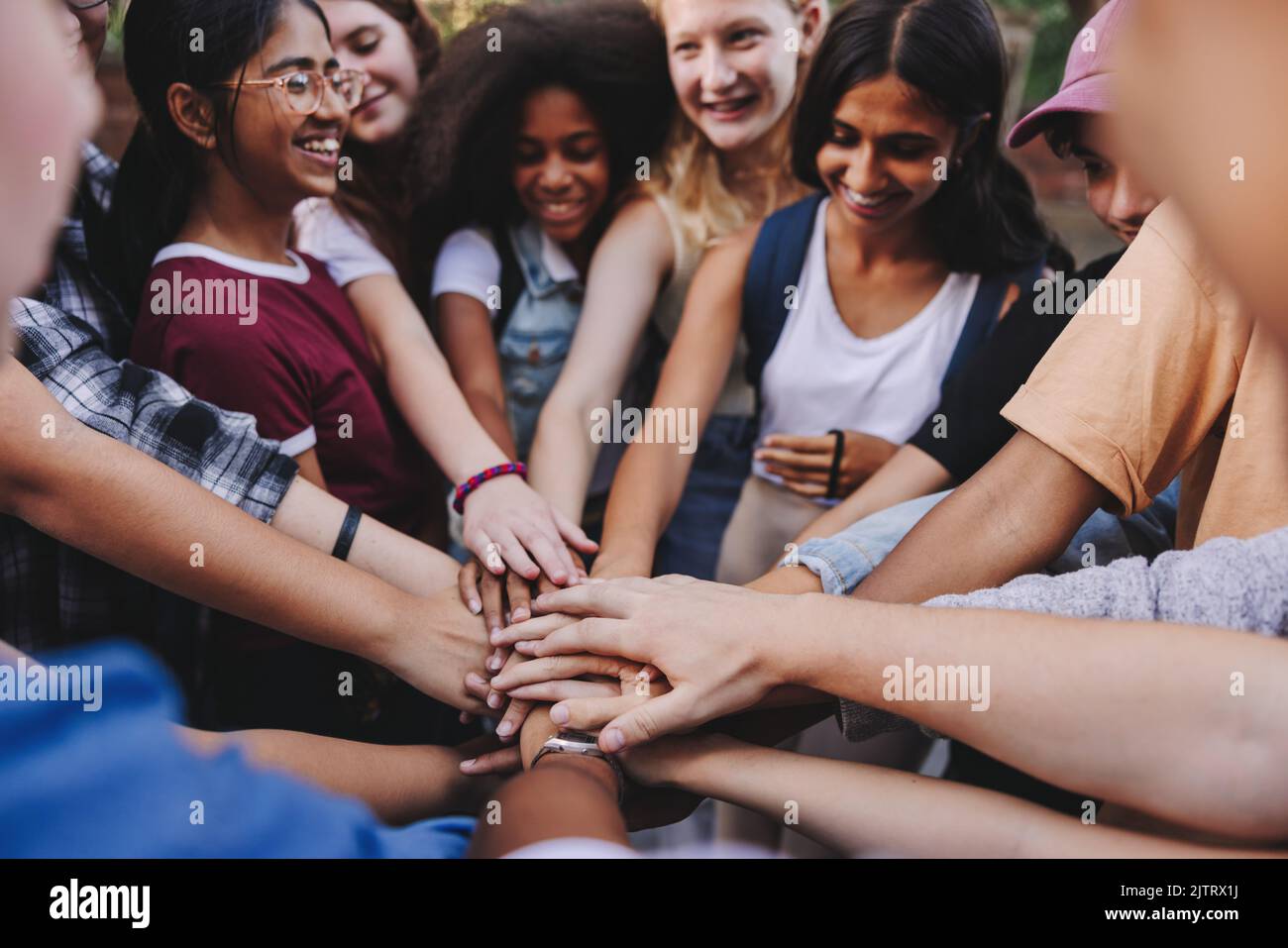 Teenager lächeln fröhlich, während sie ihre Hände in einer Hudle zusammenlegen. Gruppe multikultureller Studenten, die einen Stapel Hände bilden Stockfoto