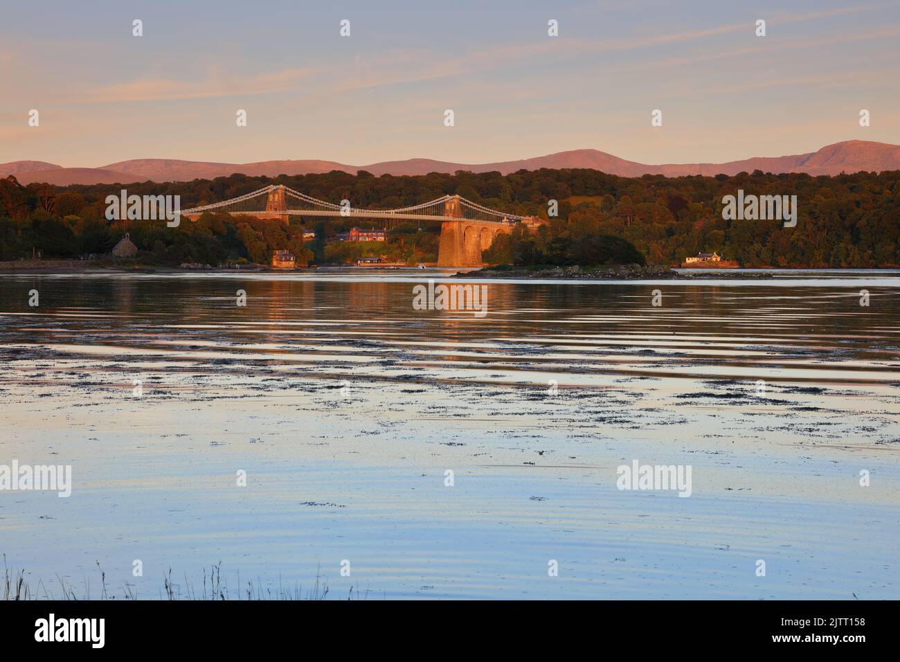 Die Menai Suspension Bridge badete in warmes Abendlicht mit den Snowdonia Mountains im Hintergrund. Anglesey, Nordwales, Großbritannien. Stockfoto