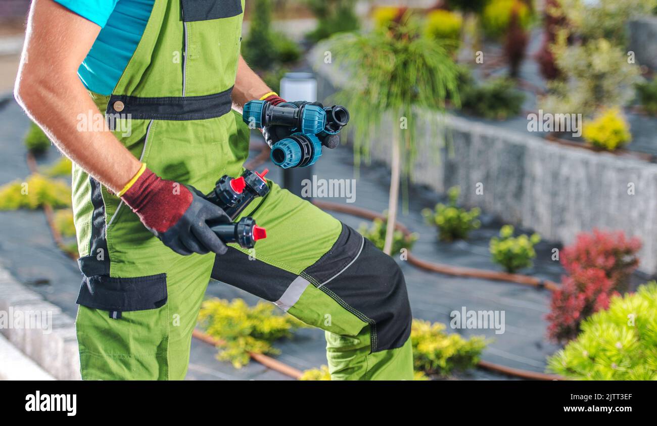 Professioneller Landschaftsgärtner, der Steckverbinder und Sprinkler in der Hand hält, während er ein Garten-Drip-Bewässerungssystem baut und installiert, um eine automatische Installation zu gewährleisten Stockfoto
