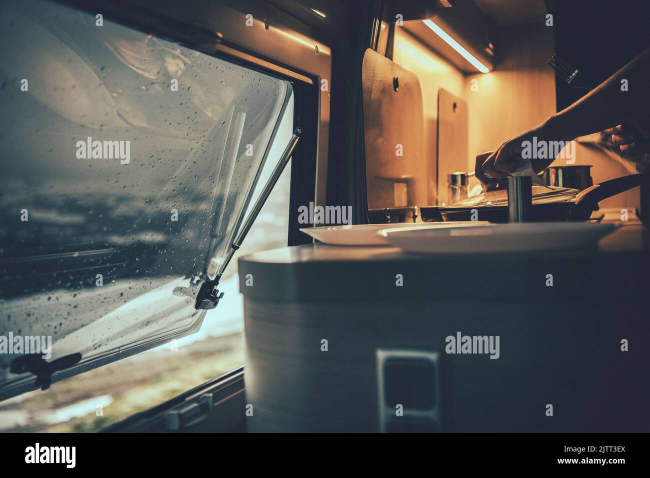 Nahaufnahme einer Person Kochen Abendessen in seinem Wohnmobil mit Küche Lichter an und Fenster leicht geöffnet. Gemütliche Abende im Wohnmobil. Lifestyle Für Reisende. Stockfoto