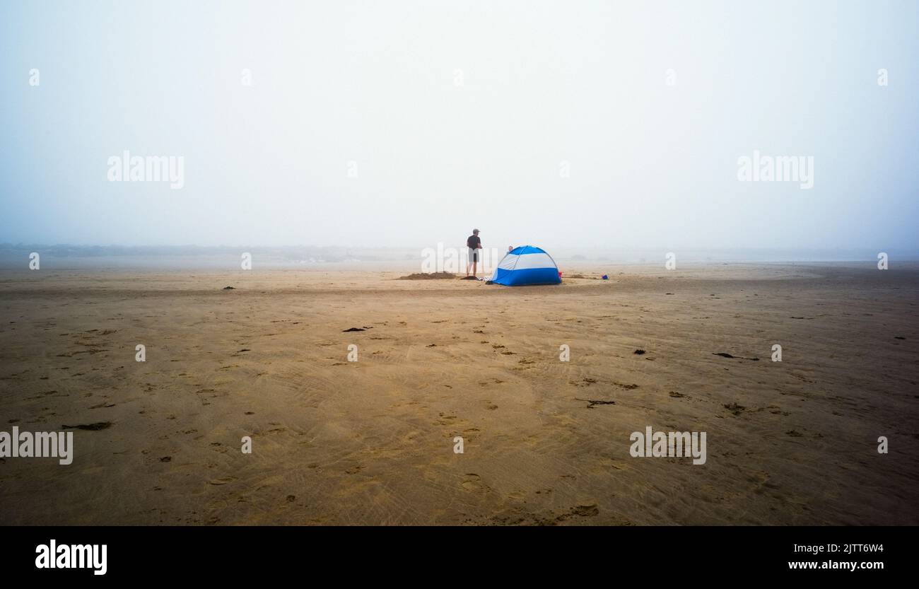 Mann und kleiner Junge mit einem blauen Zelt am Strand von Cayton Bay North Yorkshire an einem nebligen Sommertag Stockfoto