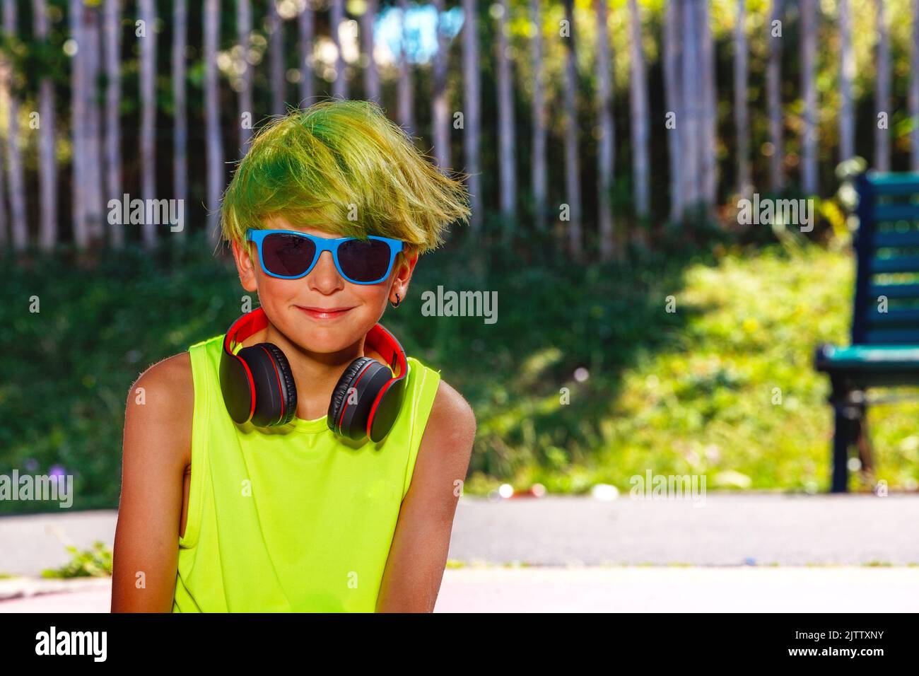 Junger Jugendlicher mit grünen Kopfhörern und Schattierungen im Park Stockfoto
