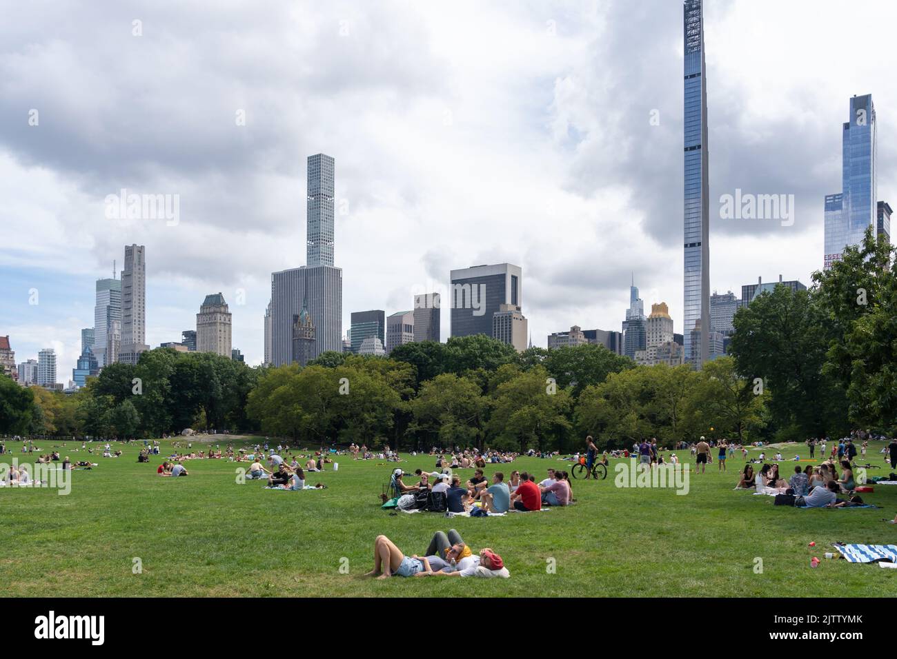 New York City, USA - 21. August 2022: Menschen entspannen sich auf dem Gras auf der Sheep Meadow des Central Park mit Gebäuden im Hintergrund in New York City. Stockfoto