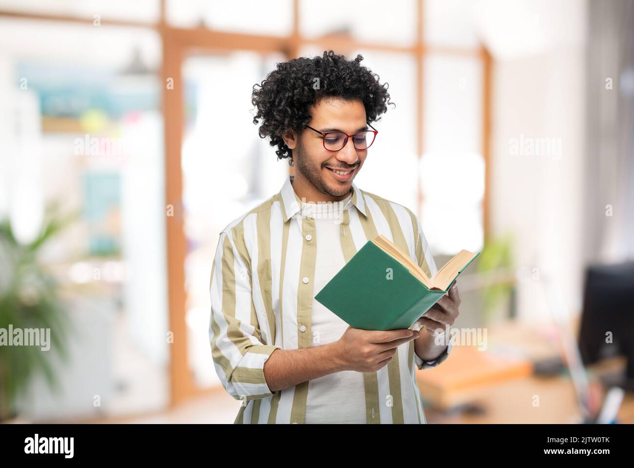 Glücklicher junger Mann in einer Brille beim Lesen des Buches im Büro Stockfoto