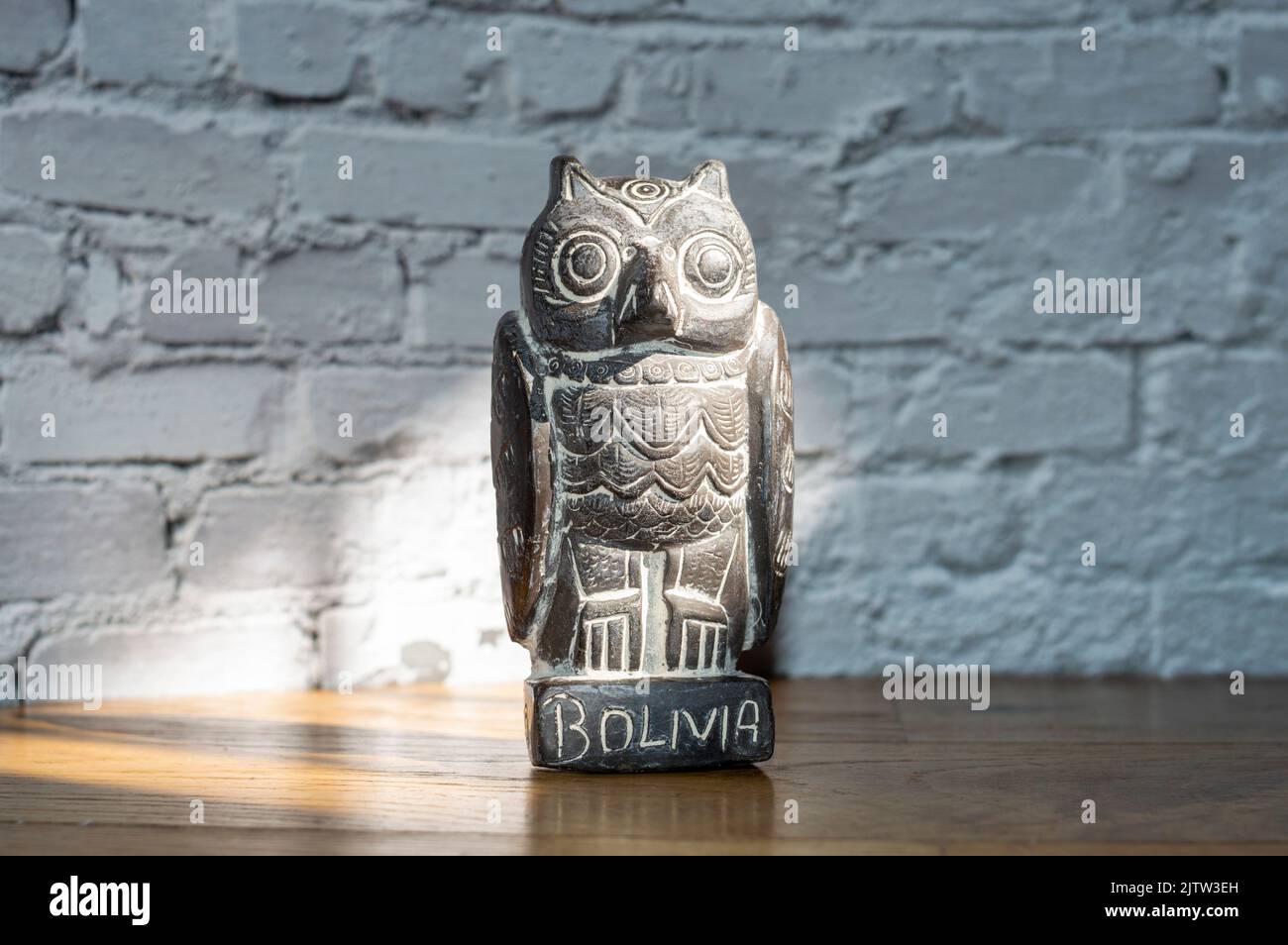 Nahaufnahme der traditionellen bolivianischen Eulenstatuette, isoliert auf einer weißen Backsteinmauer Stockfoto