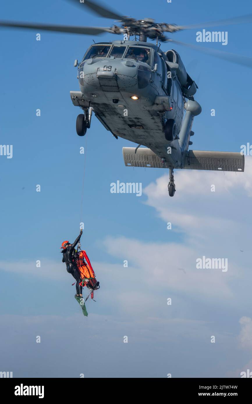 220825-N-EV253-1485 SAN DIEGO (AUG 25, 2022) – US Naval Aircrewmen, die dem Chief of Naval Operations (CNO) Search and Rescue Model Manager (SARMM) der Helicopter Sea Combat Squadron (HSC) 3 zugewiesen wurden, heben während einer dynamischen Machbarkeitsstudie in Glorietta Bay in Coronado, Kalifornien, einen Übungsdummy an einen MH-60s Seahawk Hubschrauber. 25. August 2022. Während der Evolution testete SARMM die Praktikabilität der Verwendung von zwei Rettungsschwimmern im Vergleich zu dem herkömmlichen, sowie die alternative Streu- und Bergemethode, um die Zeit zu verkürzen, die für eine Rettung erforderlich ist, und eine zukünftige fli zu erhalten Stockfoto