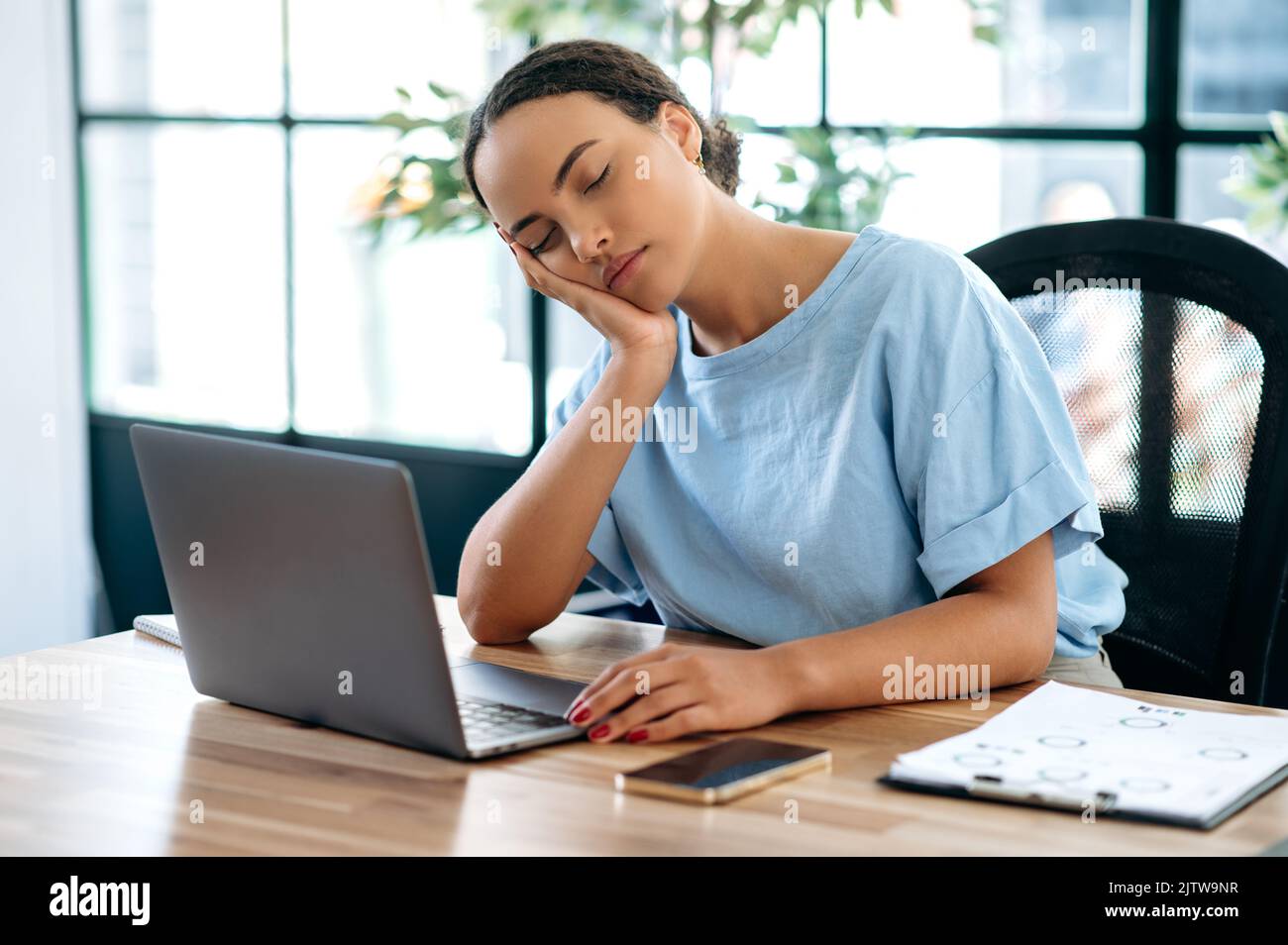 Schläfrig müde überarbeitete brasilianische oder hispanische Geschäftsfrau, Büroangestellte, die mit einem Laptop im Büro am Tisch saß, auf ihrem Arm gelehnt einschlief, chronischen Schlafentzug erlebte, Ruhe brauchte Stockfoto