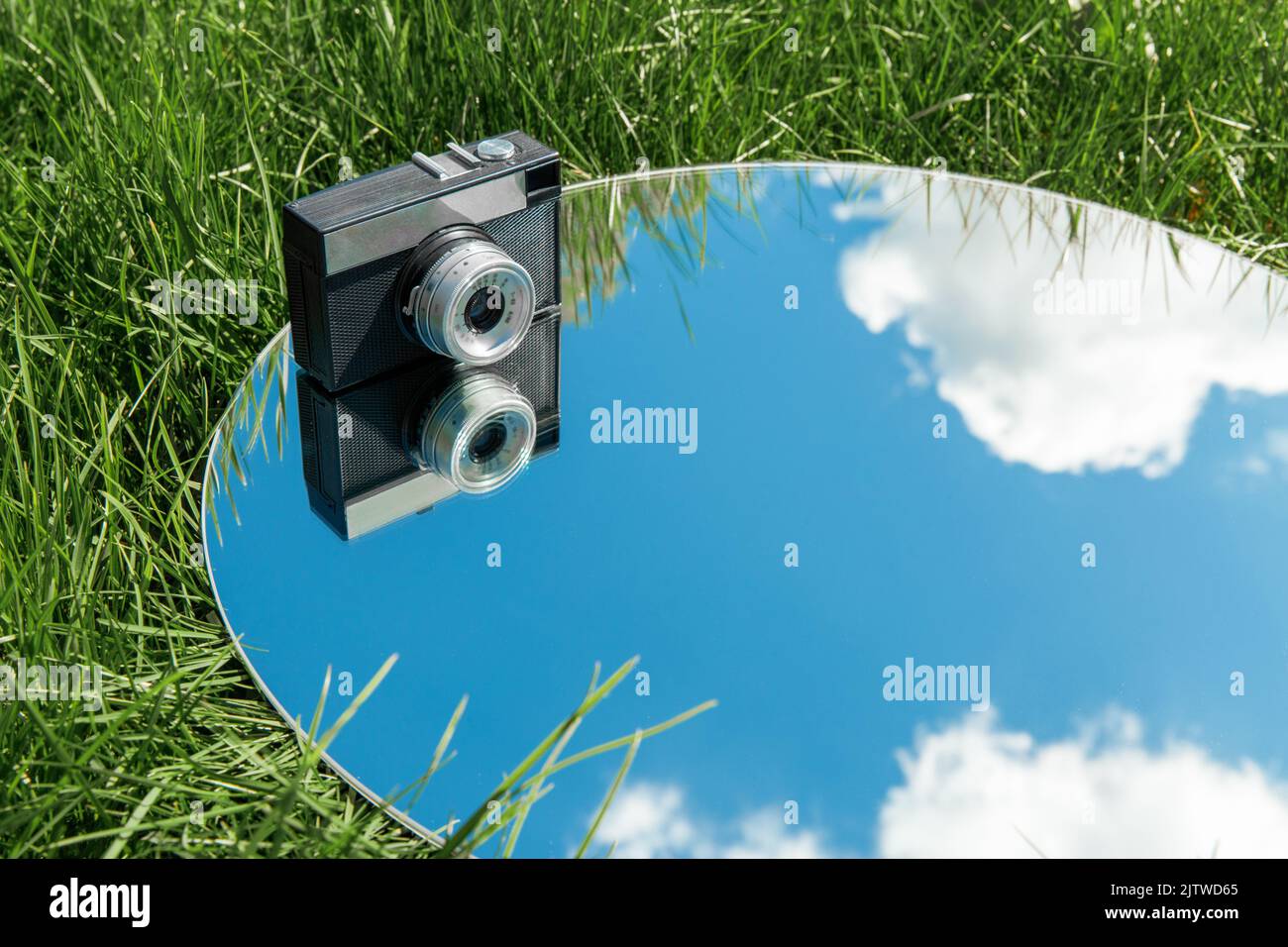 Spiegelung von Kamera und Himmel im runden Spiegel auf Gras Stockfoto