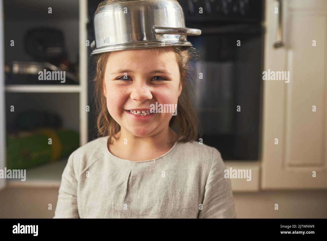 Gefällt dir mein ausgefallener Hut? Beschnittenes Porträt eines kleinen Mädchens, das einen Topf auf dem Kopf trägt. Stockfoto