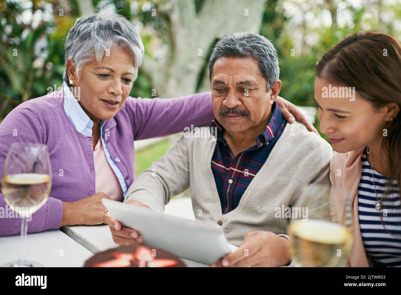 Herausfinden der Feinheiten der sozialen Medien. Ein älterer Mann zeigt seiner Familie etwas auf seinem Tablet, während sie draußen zu Mittag essen. Stockfoto