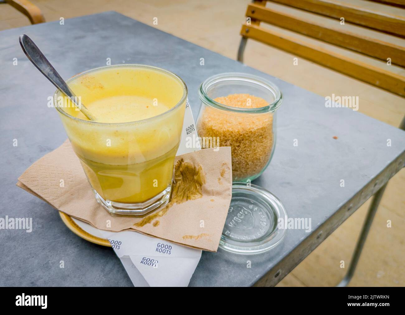 Süßer, gelb getönter Kaffee, serviert in einem Glas, mit einem Löffel, nachdem er mit demerara-Zucker gerührt wurde, auf einem Restauranttisch im Freien. Stockfoto