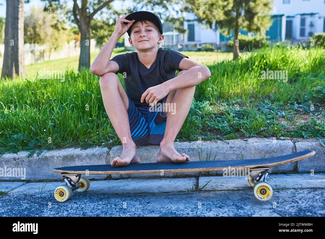 Ich und mein Longboard. Porträt eines Jungen, der mit seinem Longboard auf der Bordsteinkante sitzt. Stockfoto