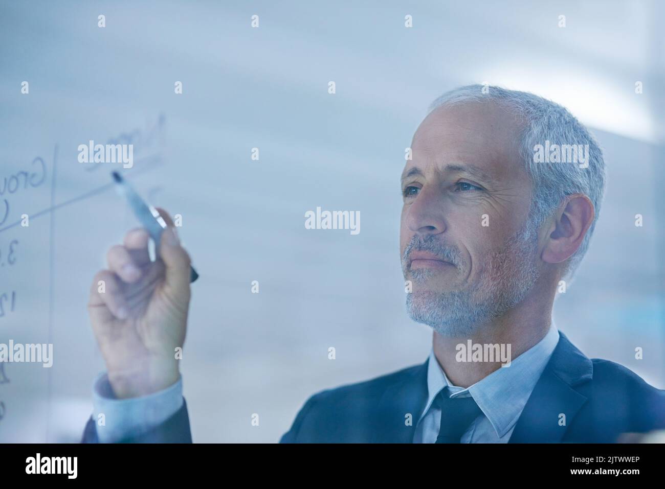 Arbeiten mit Genauigkeit. Ein reifer Geschäftsmann, der Figuren auf einem Glasschirm schreibt. Stockfoto