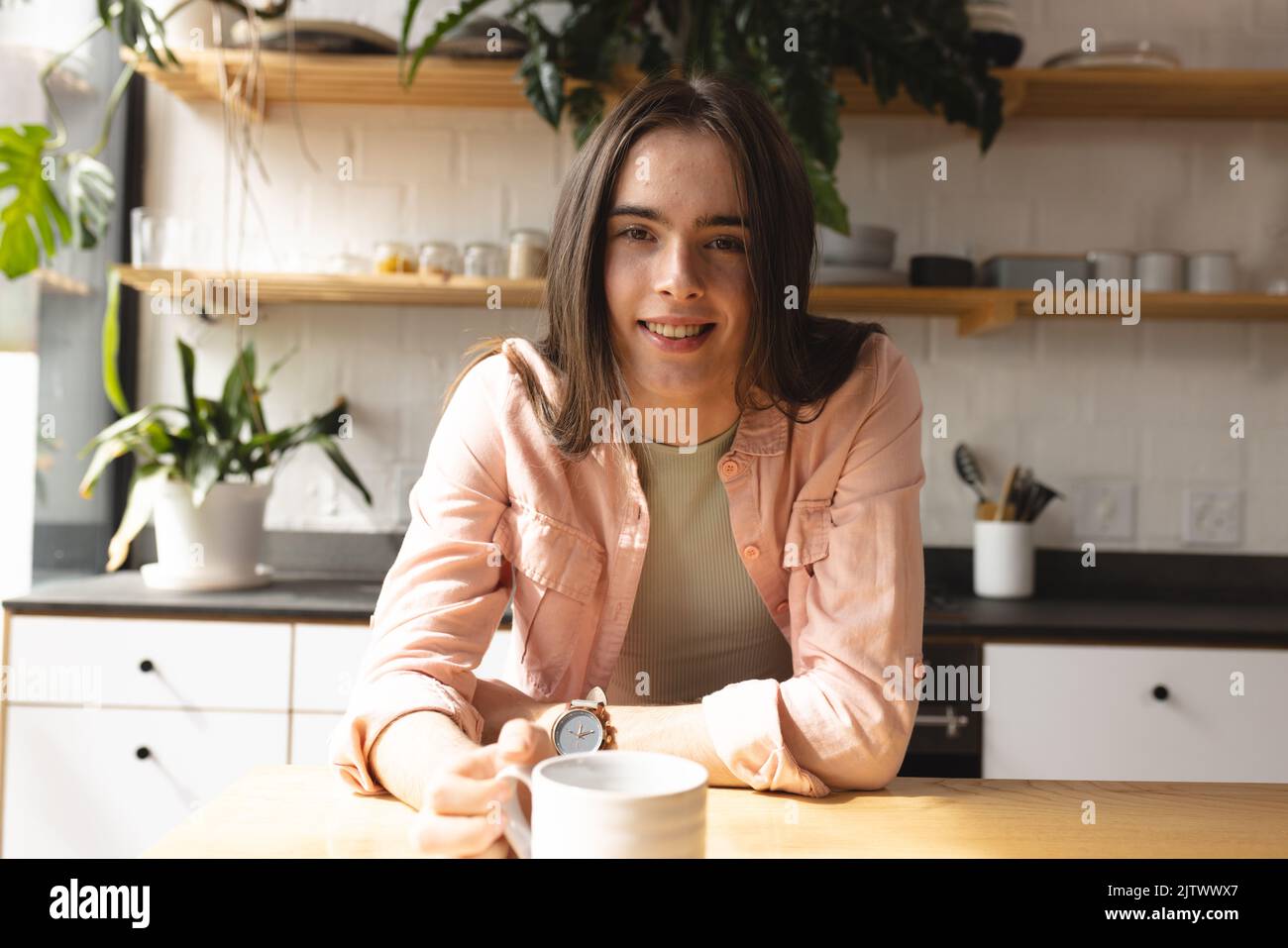 Porträt einer nicht-binären Transfrau mit lächelnder Kaffeetasse in der Küche zu Hause Stockfoto