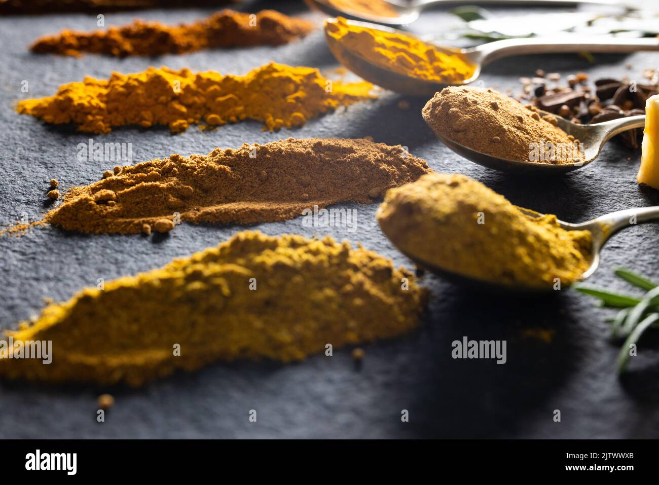 Blick aus der Höhe auf Löffel mit verschiedenen gemahlenen Gewürzen auf dem schwarzen Marmortisch Stockfoto