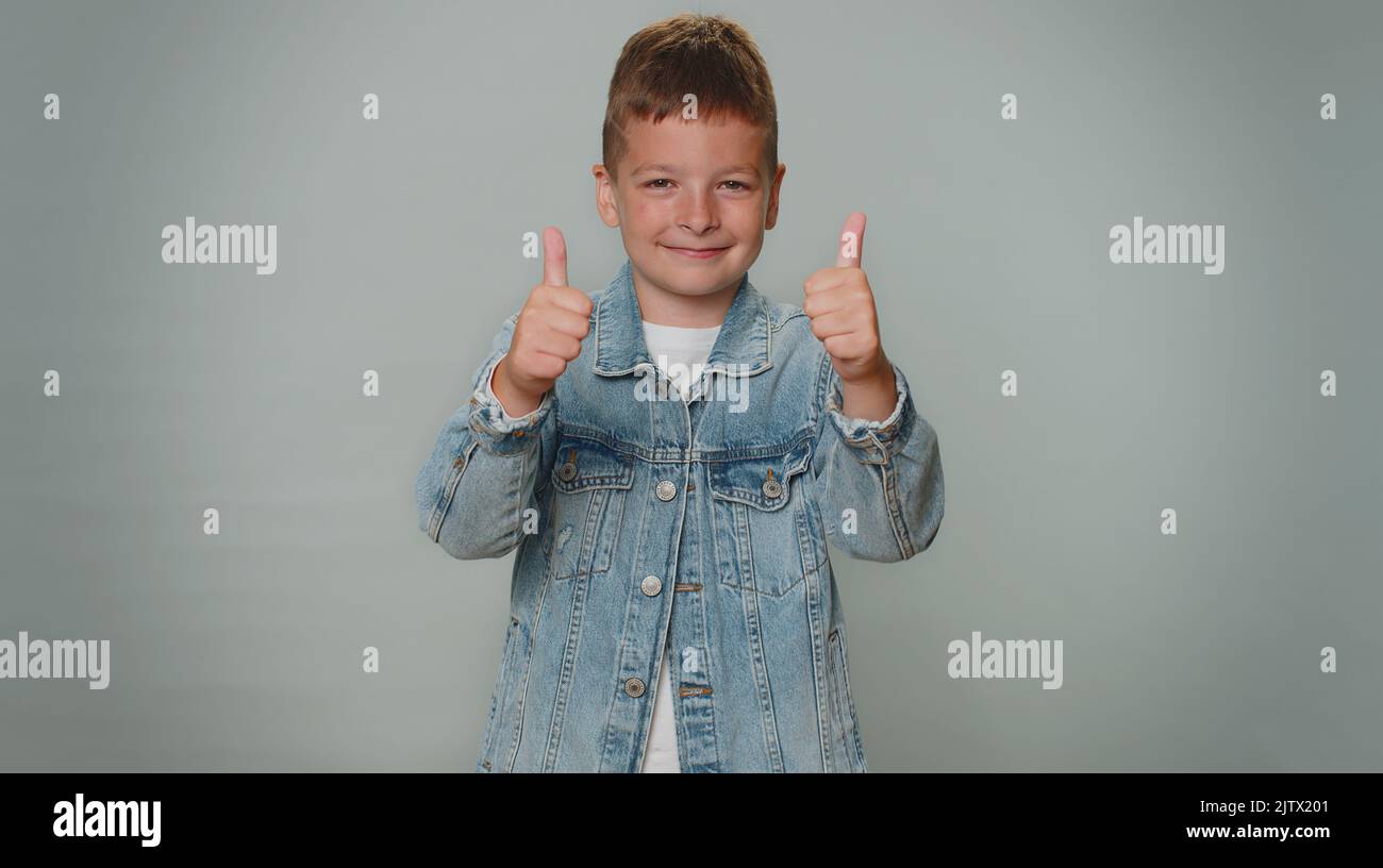 Tolle Arbeit. Fröhlich positiv glücklich Junge in der Jacke zeigt Daumen nach oben und nickt in Zustimmung, erfolgreiche gute Arbeit. Junge stilvolle Kinder Teenager Kind auf grauem Hintergrund. Menschen aufrichtige Emotionen Stockfoto